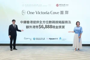 Two presenters stand on a stage in front of a large screen reading One Victoria Cove with Chinese text and sponsor logos visible