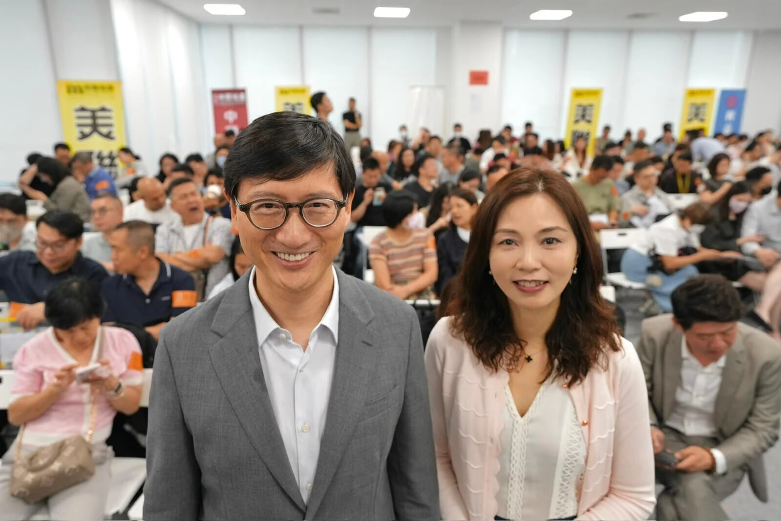 Smiling man in a gray suit and a woman in a light blouse pose at the front of a crowded conference room