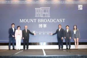 Seven professionals in formal attire stand on a stage in front of a blue backdrop reading MOUNT BROADCAST with company logos posing for a photo
